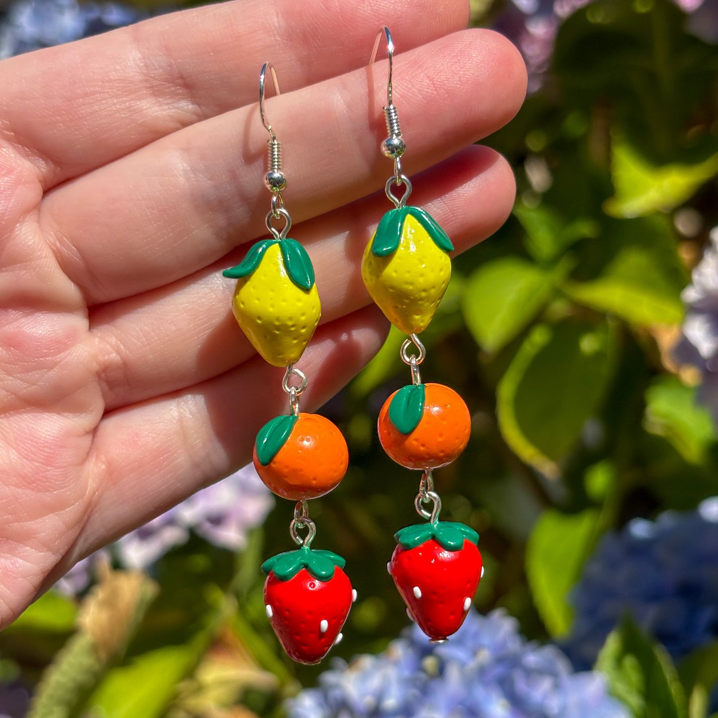 Colorful fruit-shaped earrings held against a floral background