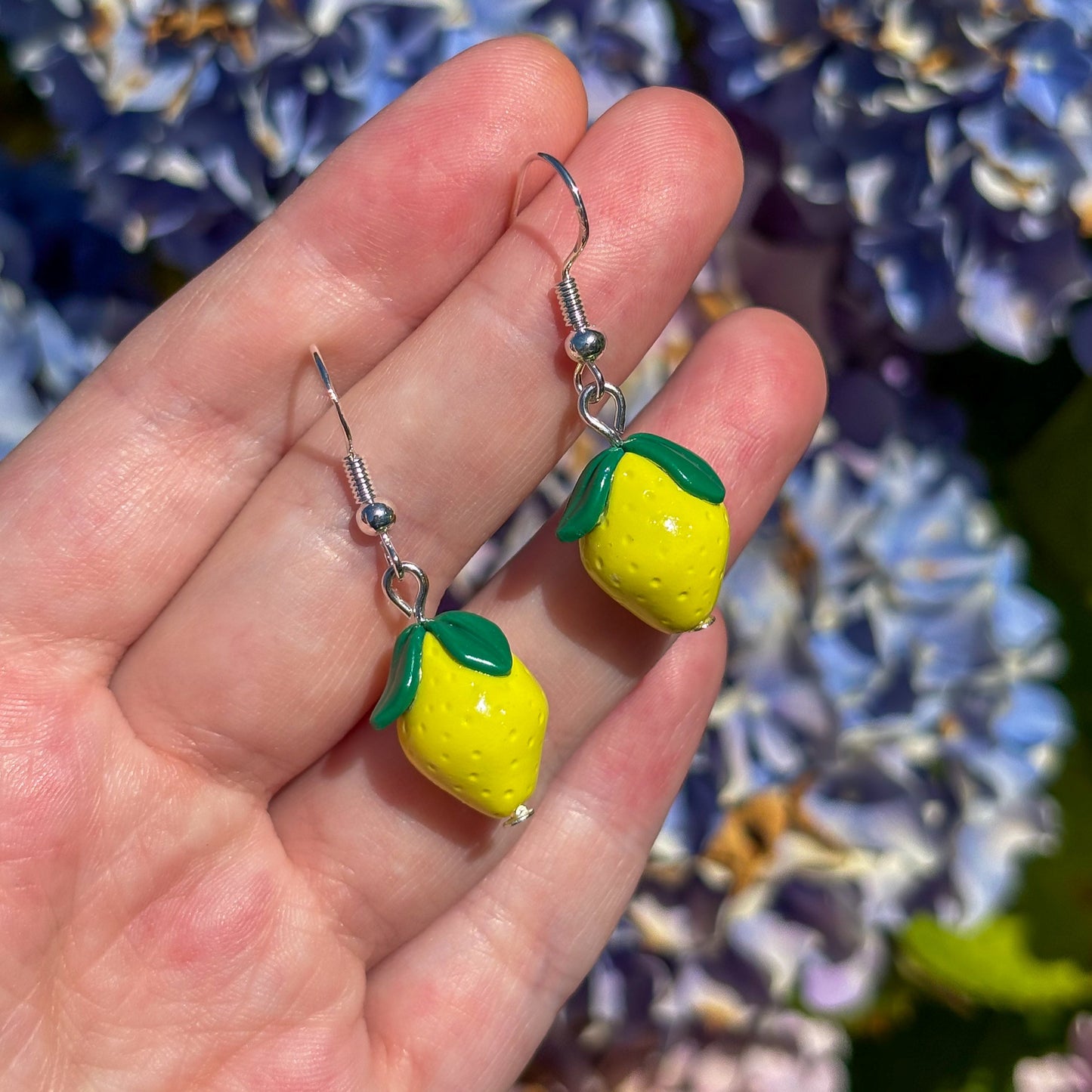 Lemon-shaped earrings held in front of a floral background