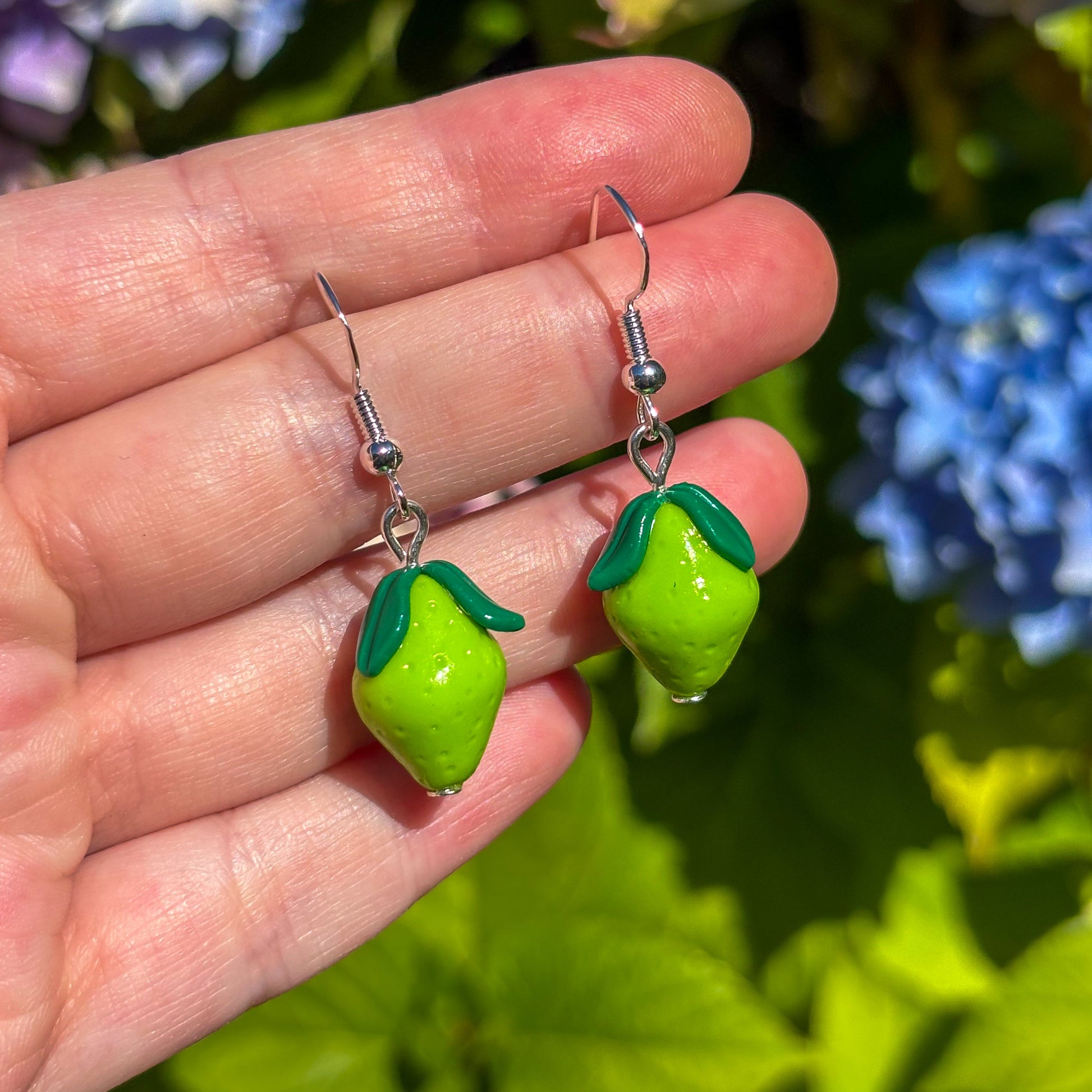 Green lime-shaped earrings held in a hand with a floral background
