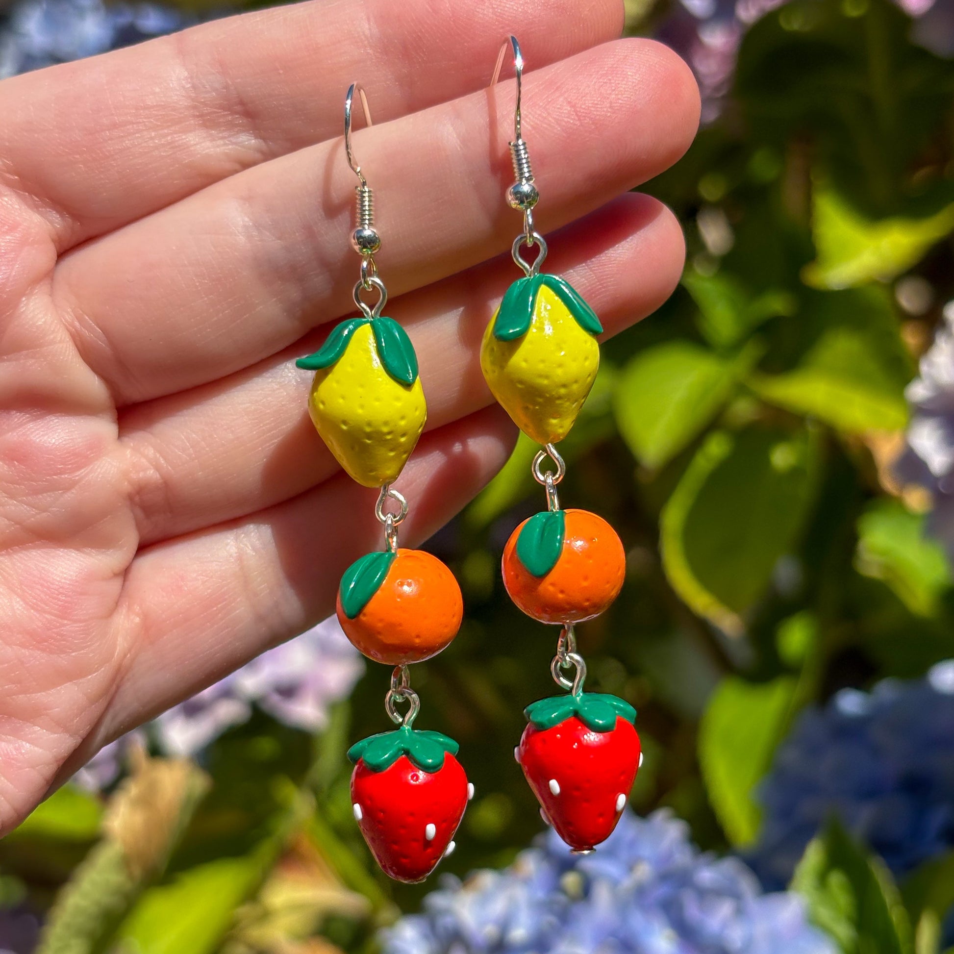 Colorful fruit-shaped earrings held against a floral background