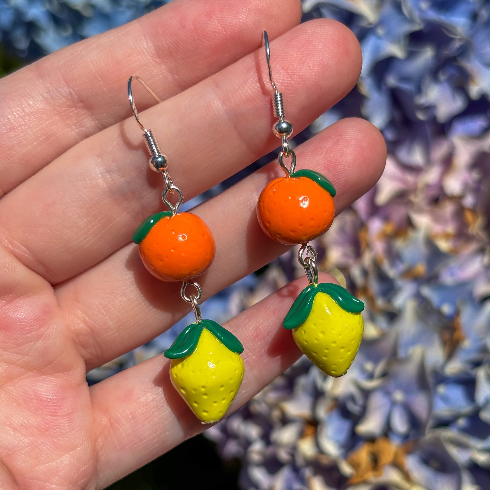 Lemon and orange earrings held in a hand with a floral background