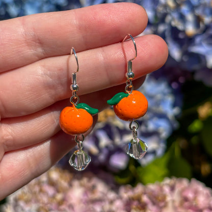 Orange earring with green leaves held against a floral background
