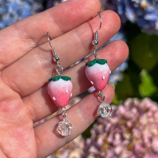 Hand holding strawberry-shaped earrings with a floral background